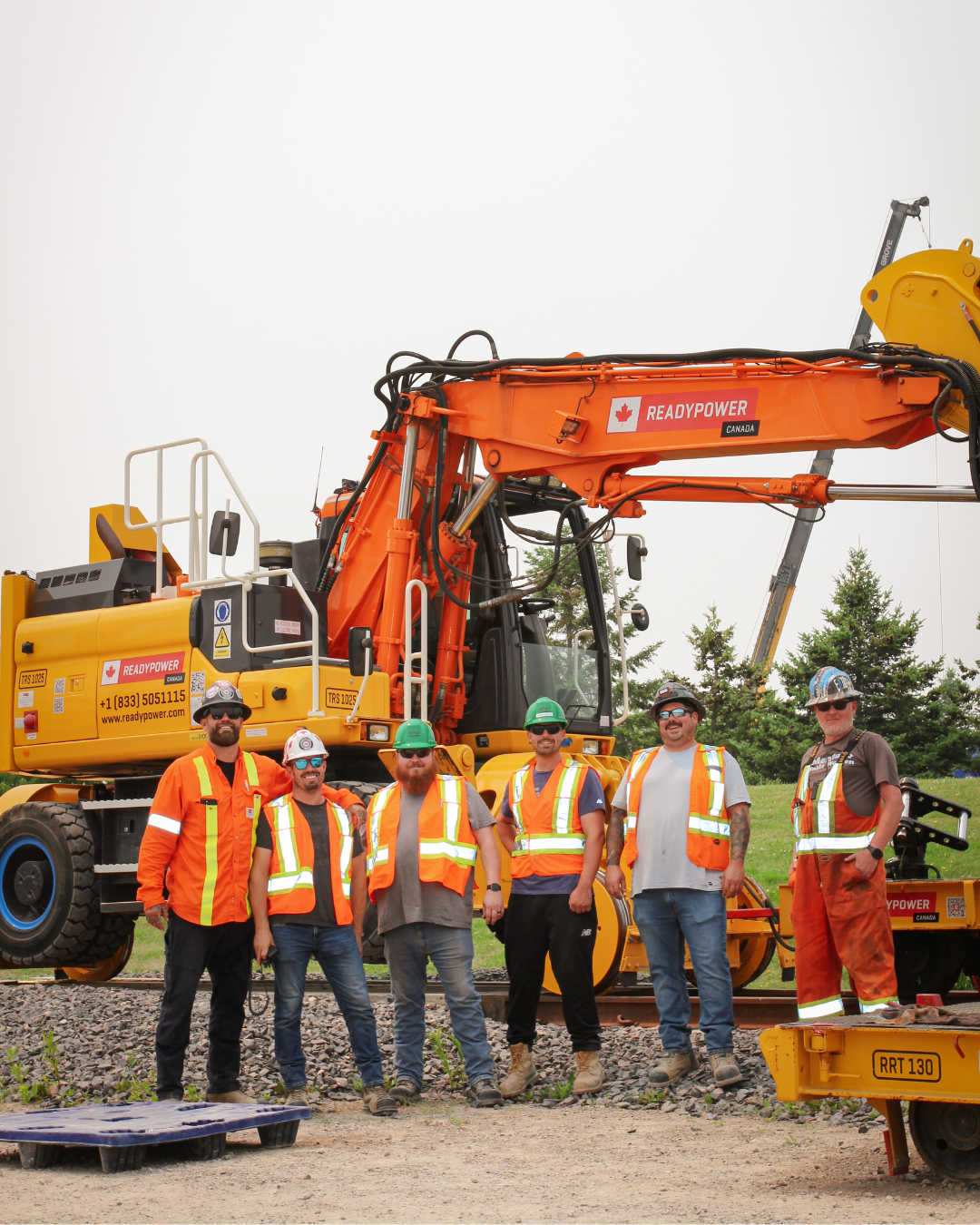 6 male operating engineers stand side by side smiling at the camera in front of a High Rail Excavator.