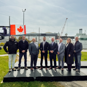 A group of men and 1 women stand side by side with the Canadian Flag behind them