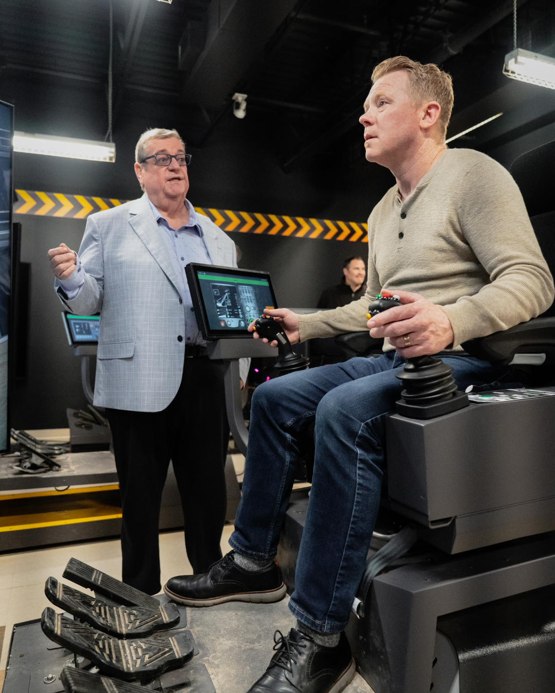 Sean O'Meara (right, sitting down) testing out a simulator machine with 793 Business Manager Mike Gallagher (left) watching over