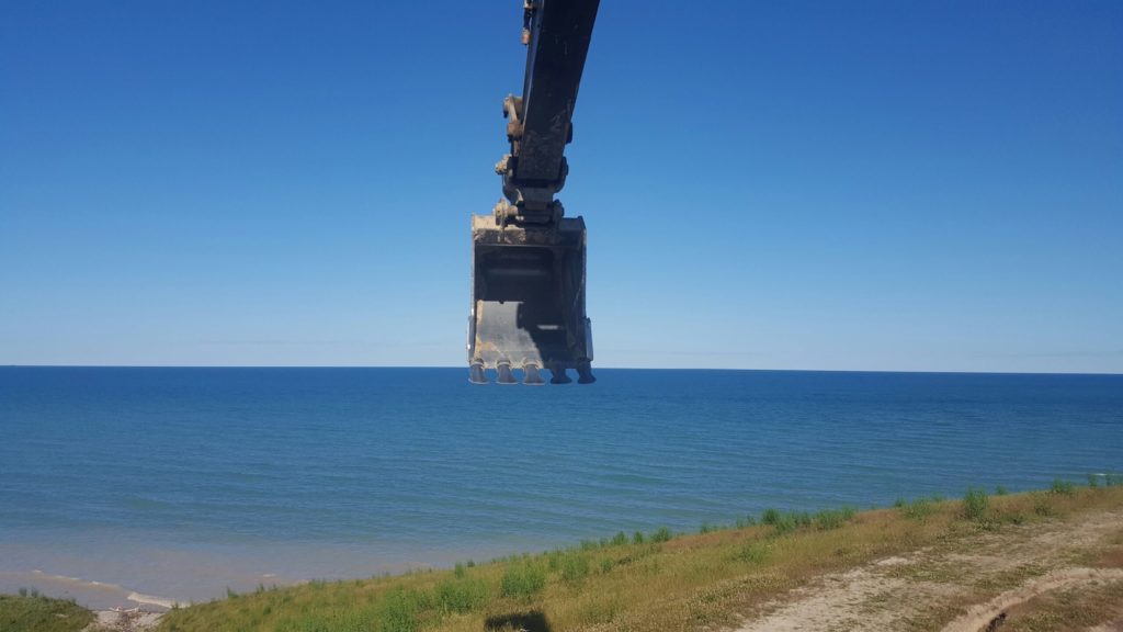 Brother Robert Scott operates his excavator on the shores of a sun-kissed Lake Huron.