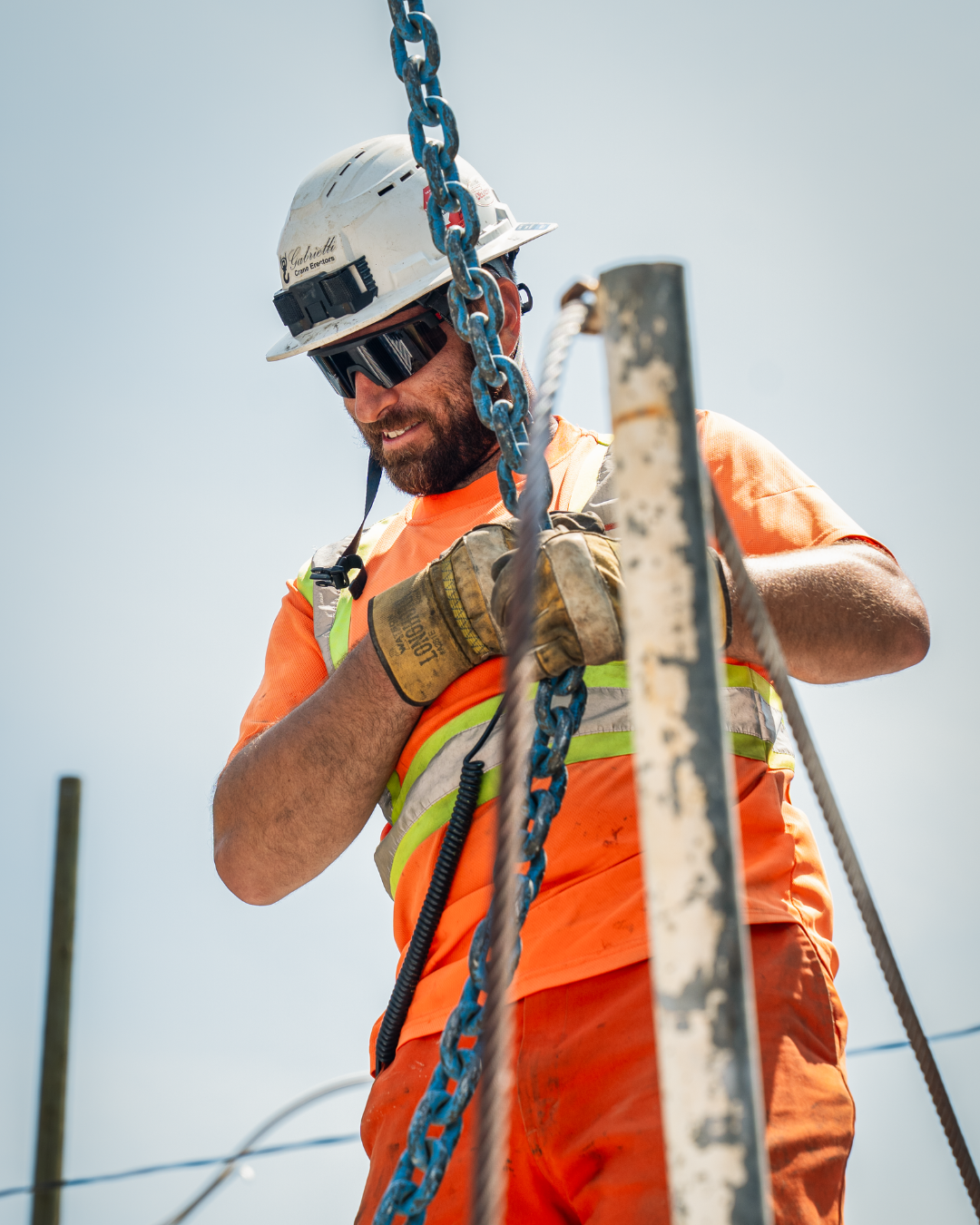 A construction working with a white helmet and sunglasses holding a blue chain