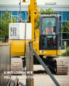 An image of an apprentice in a yellow mobile crane holding a 520lbs cement block. Text in the bottom left corner of the image reads: Always learning new skills to build better.