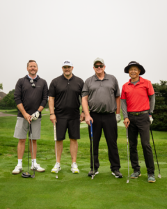Justin O'Neill (left), Bob Brooks, (middle left), Dave Turple (middle right) and Ken Lew (right) stand side by side smiling on a golf course.