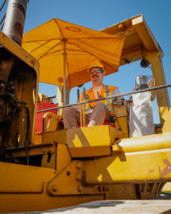 A man in P.P.E sitting onto a piece of yellow machinery.
