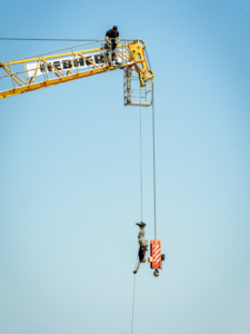A man rappelling upside down off the boom of a crane