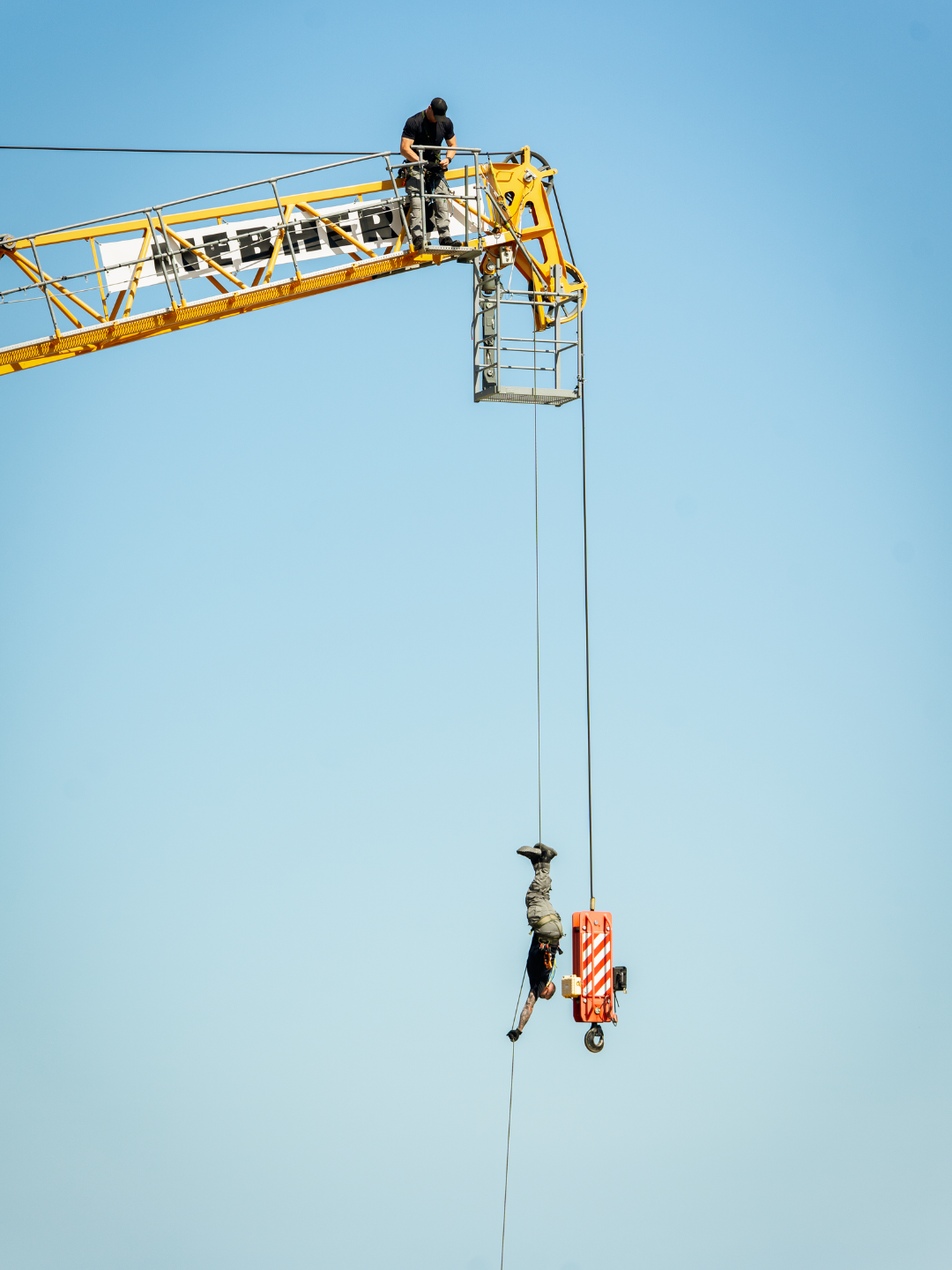 A man rappelling upside down off the boom of a crane