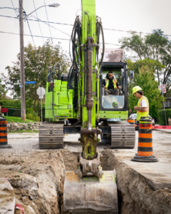 a green excavator lifting dirt from a hole in the ground.