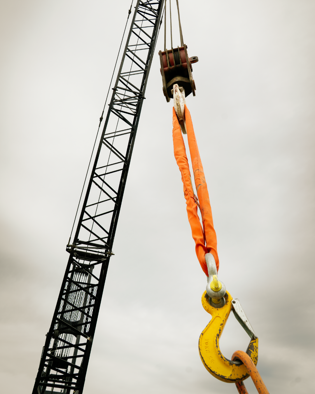 the mast of a crane with an orange and yellow hoist hook on the end of it.