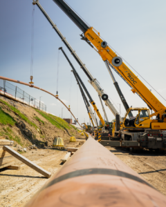 5 cranes holding up a pipe in the air