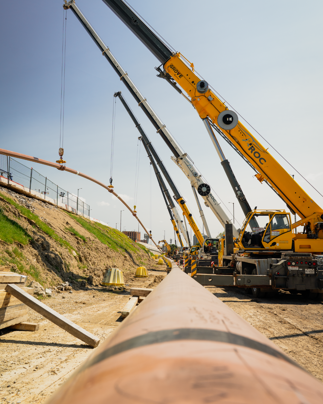 5 cranes holding up a pipe in the air