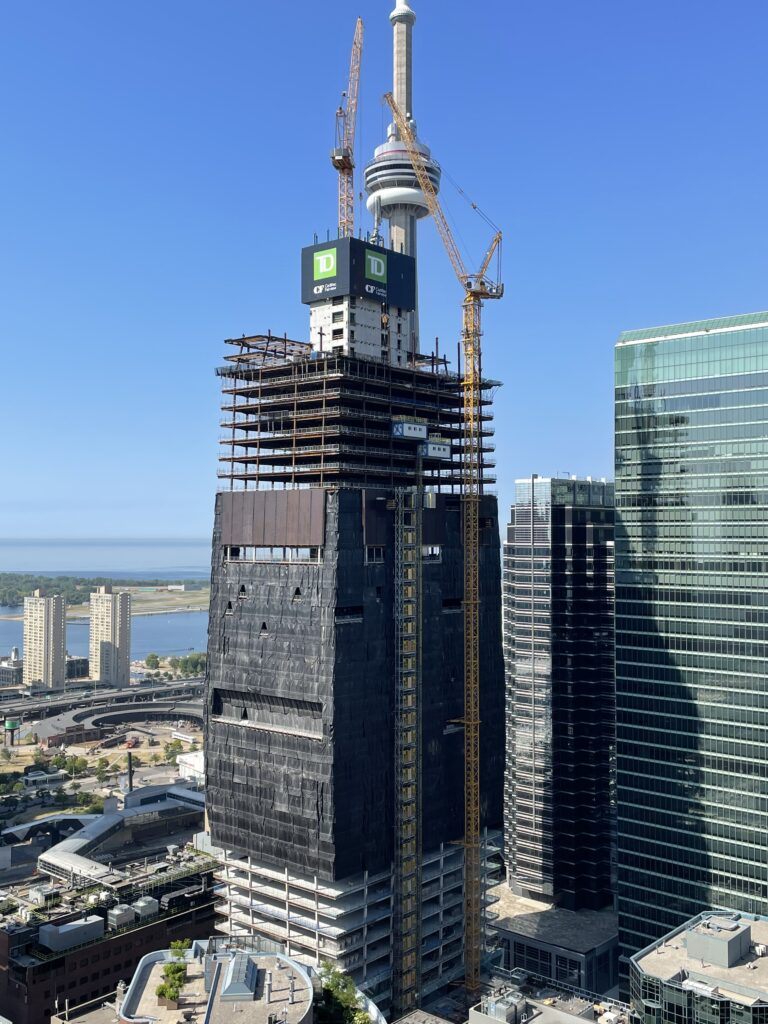 Image of TD Bank tower scaffolding with tower crane operated by member on its right side and the CN Tower in the background 