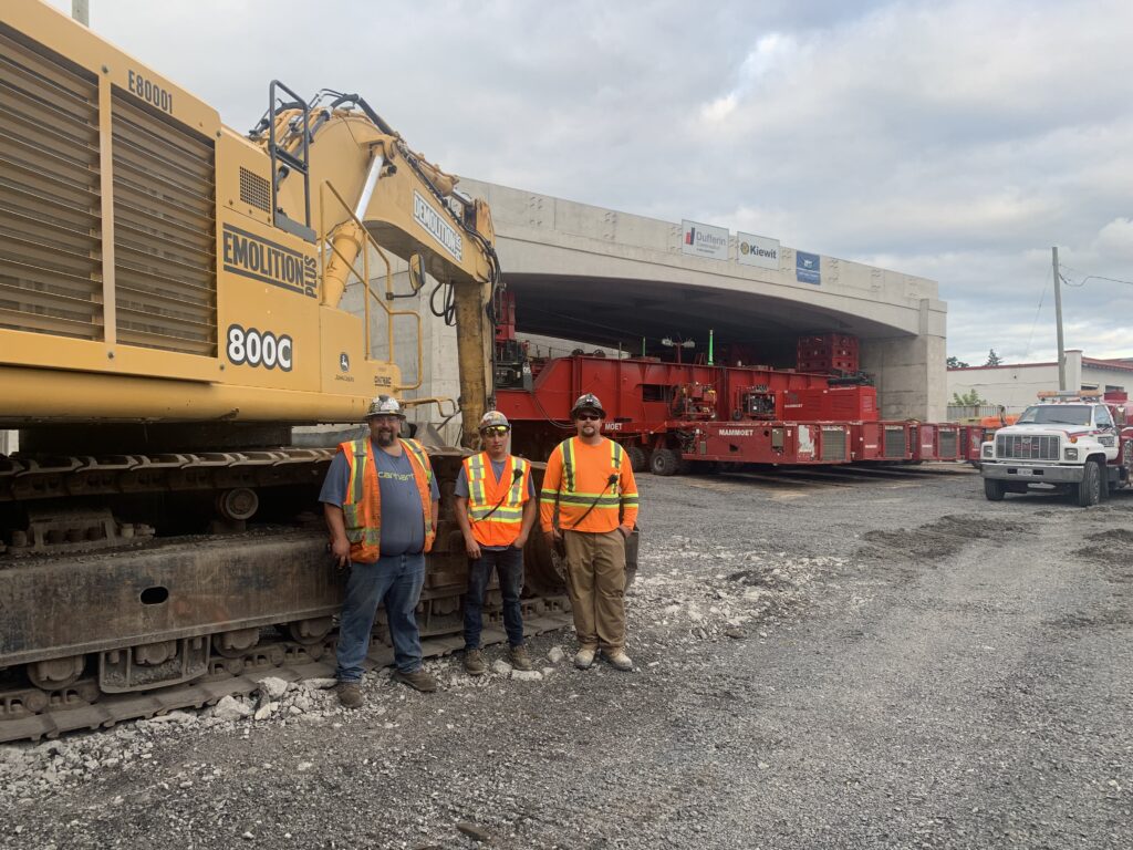 Three members on-site in front of an overpass on Highway 417