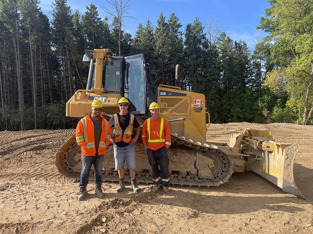 Three members standing in front of the dozer on site