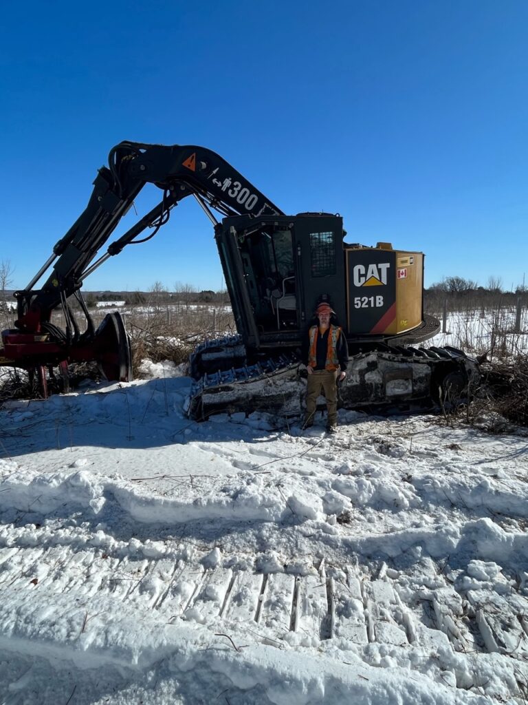 Member standing in front of excavator on the snow covered site with cleared trees in the background