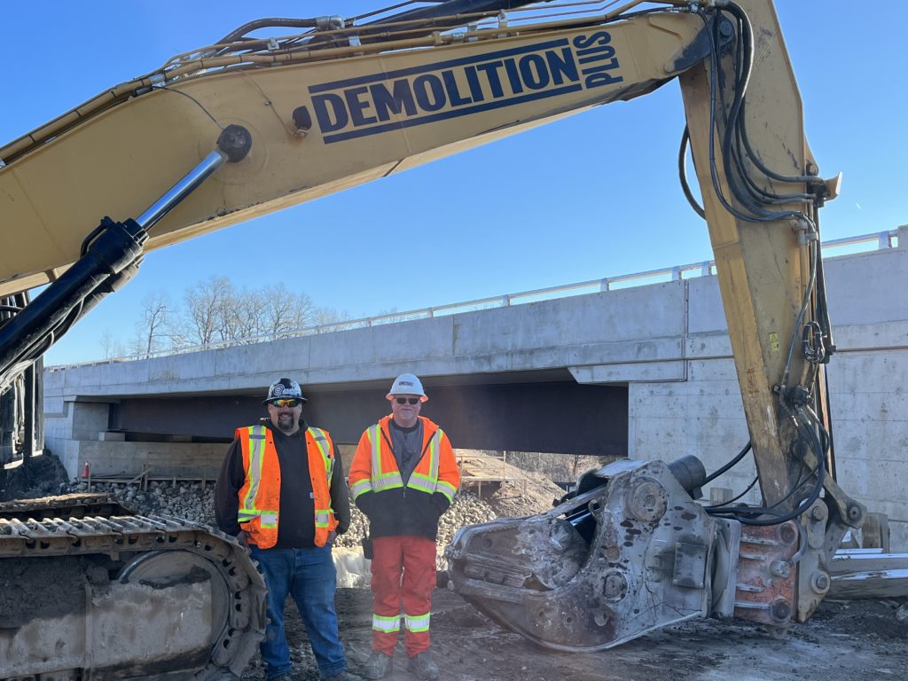 Two members standing under the neck of the excavator