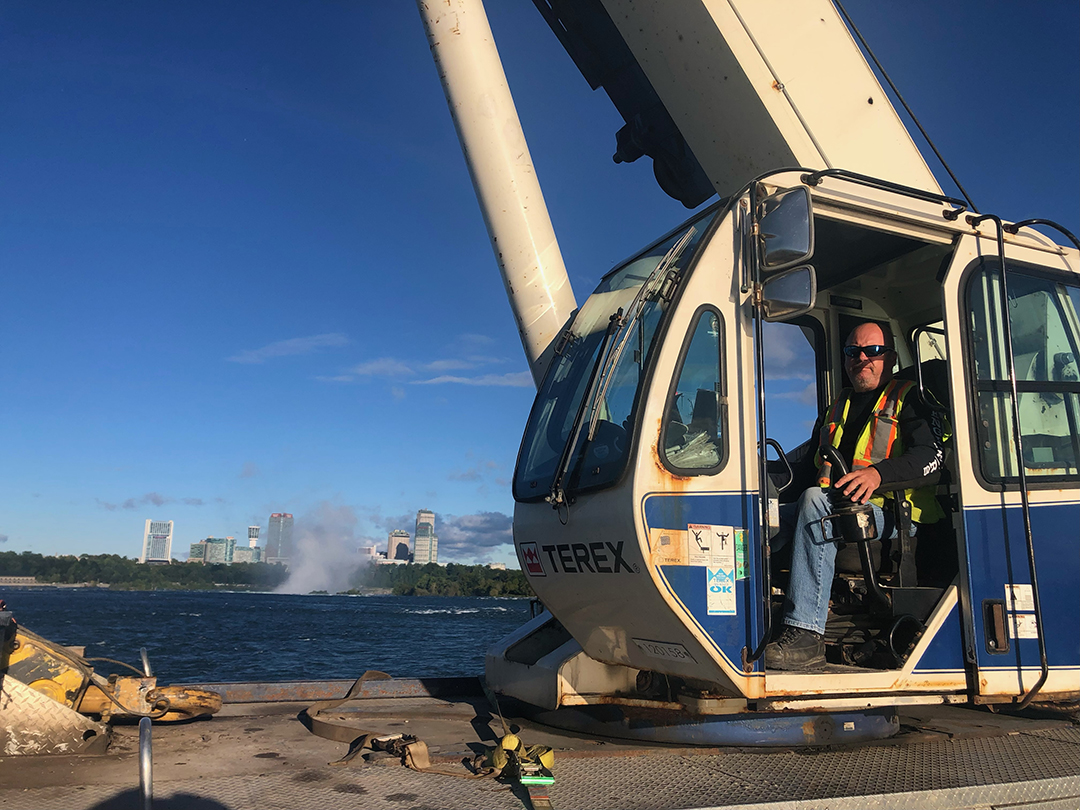 member inside crane cab with waterfront in the background