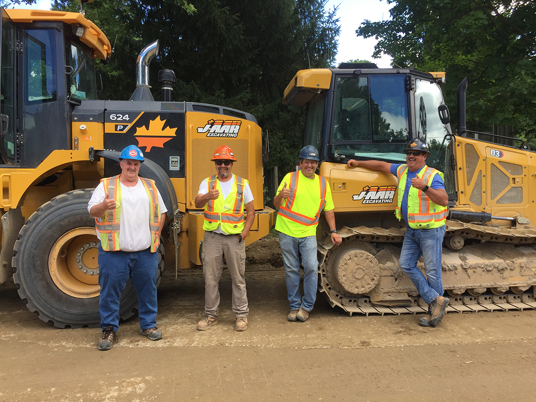 Four members give a thumbs up in front their heavy equipment 